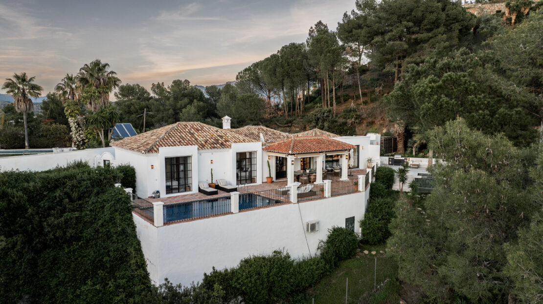 El Madroñal Villa in Benahavís with traditional Spanish cortijo design, white lime-clad walls, and red-tiled roofs, surrounded by lush greenery.