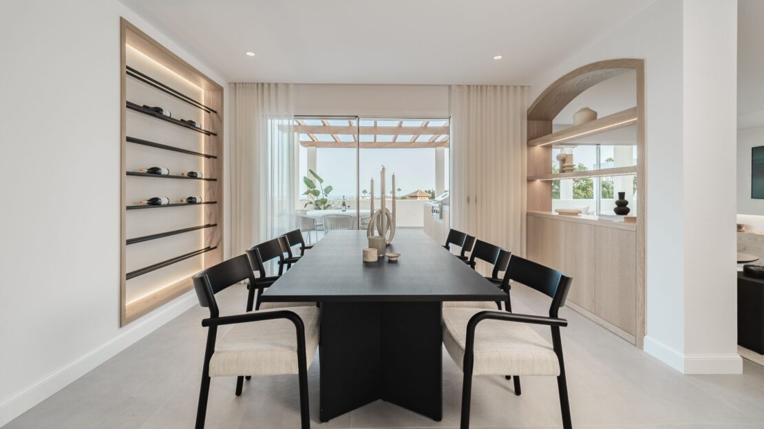 Close-up of modern six-seater dining table with adjacent doorway and ambient LED glow from integrated wine cellar in Los Belvederes penthouse, Marbella