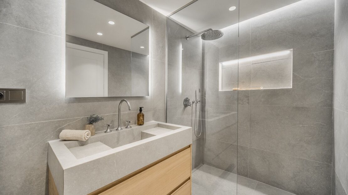 Modern bathroom with floating vanity, backlit mirror, and glass-partitioned shower in Los Belvederes penthouse, Marbella luxury home