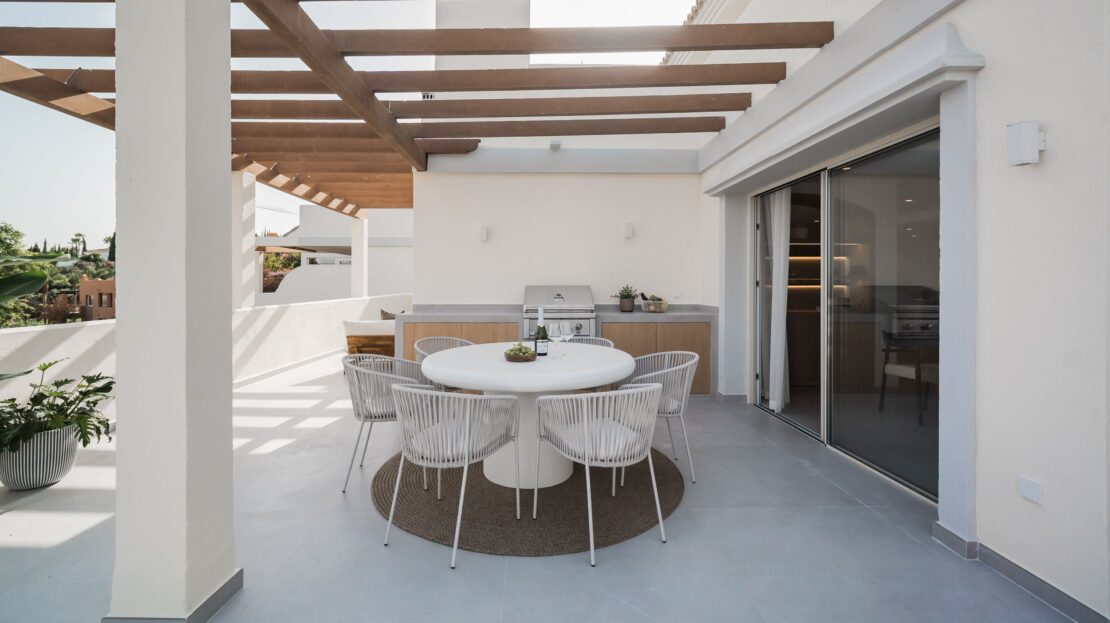 Luxury outdoor dining set under wooden canopy with Ruby grill and glass sliding doors to interior in Los Belvederes penthouse, Marbella