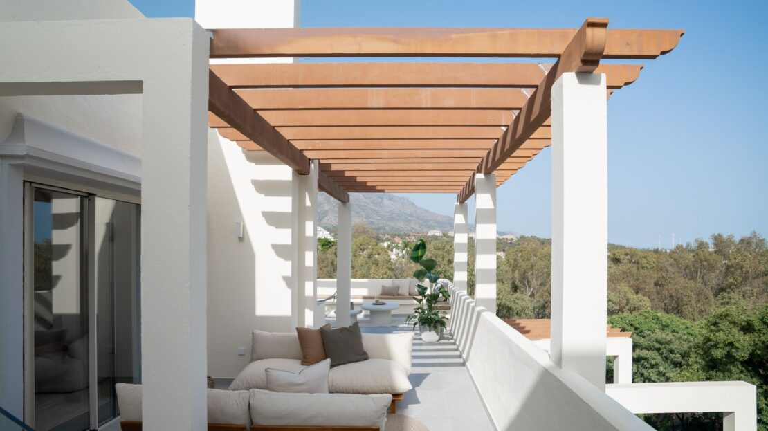 Modern penthouse rooftop lounge area with strategic pillar design offering partial shade, showcasing built-in seating and luxury furnishings in Los Belvederes, Marbella