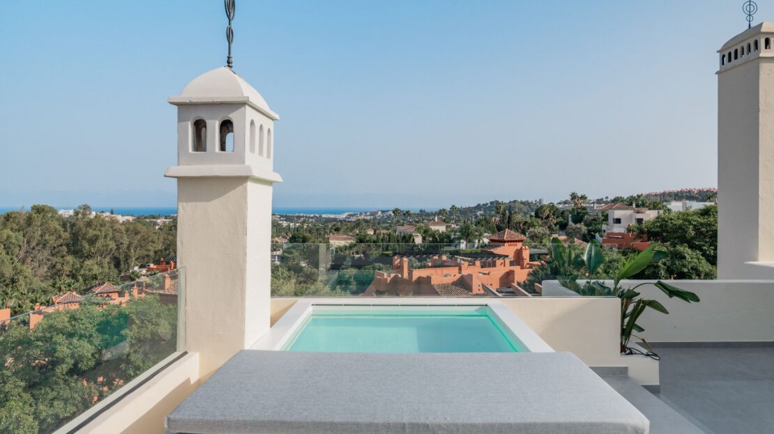 Modern glass railing and structural pillar framing panoramic sea and mountain views from Los Belvederes penthouse rooftop, Marbella luxury residence