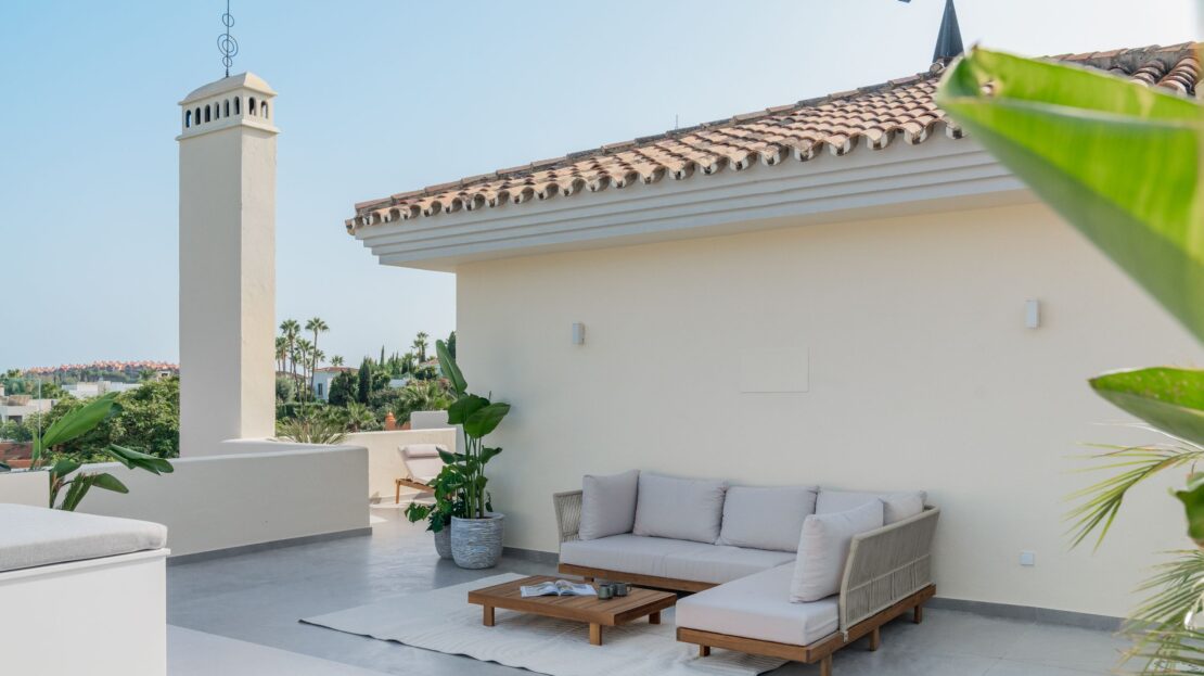 Close-up of designer rooftop couch with sleek wooden side table and minimalist carpet in Los Belvederes penthouse, Marbella luxury terrace
